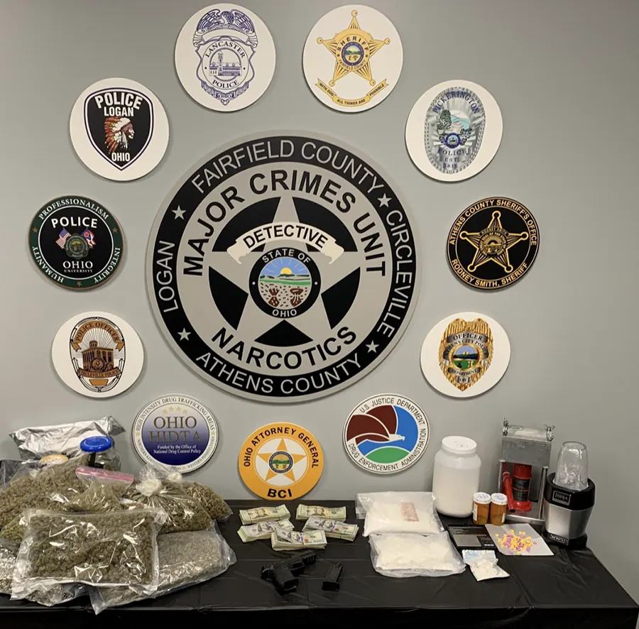 Seized marijuana, cocaine, cash, handguns and pills on a table below the Major Crimes Unit badge and partner agency logos